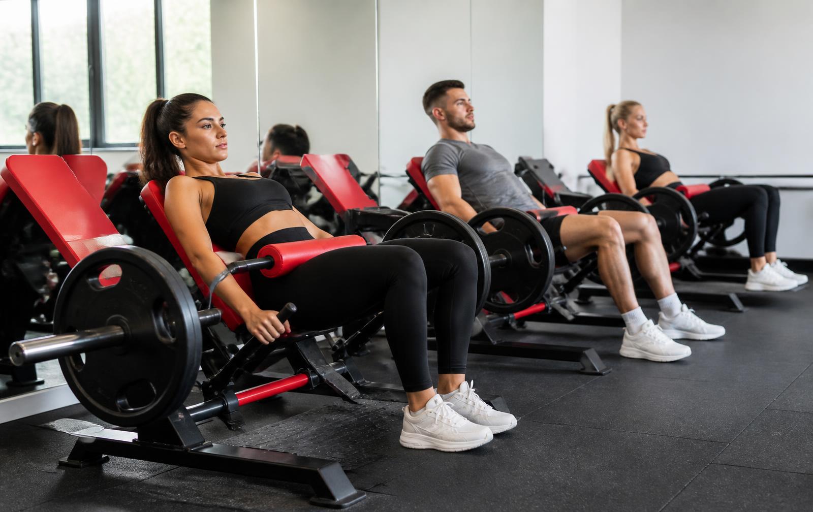 A row of red hip thrust machines in the Redwood Fitness BootyBuilder room with members training