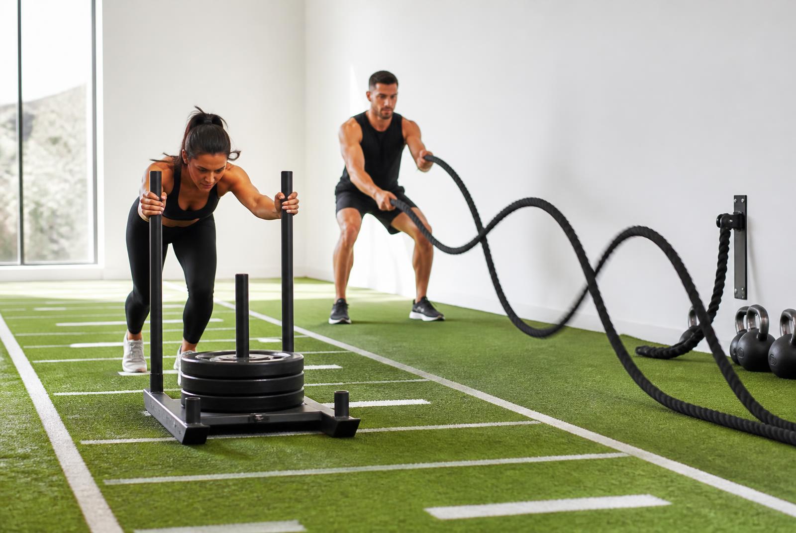 Members pushing a sled and using battle ropes on the green turf lane